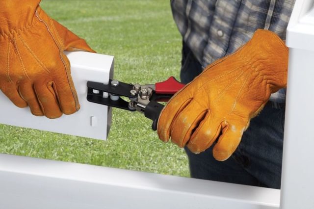 A worker wearing gloves using a malco notching tool to make tabs in a section of vinyl fencing